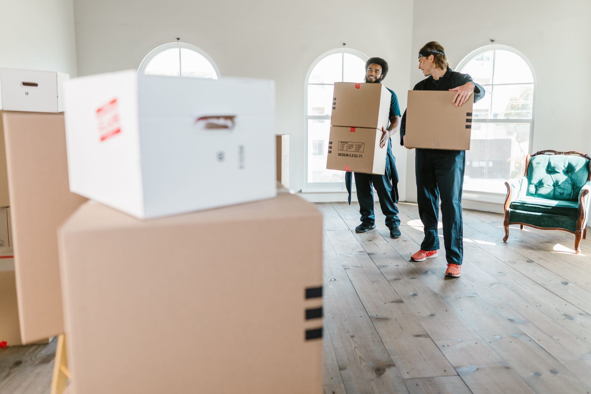 Verschiedene Kartons mit Haushaltsgegenständen und ein Koffer stehen vor dem Umzug in eine neue Wohnung auf dem Boden eines hellen Zimmers.